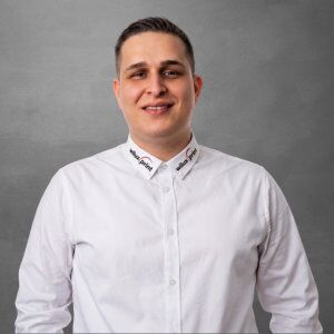Leotrim Komani, Mitglied des Teams WILUX PRINT, technischer Verkäufer für AIDC, Etikettendrucker, Software und Scanner, professionell gekleidet in einem weissen Hemd vor einem neutralen Hintergrund.